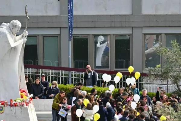 Niños sosteniendo globos blancos y amarillos se reúnen junto a la estatua de Juan Pablo II fuera del Hospital Universitario Gemelli, donde el Papa Francisco está hospitalizado, en Roma el 16 de marzo de 2025.
