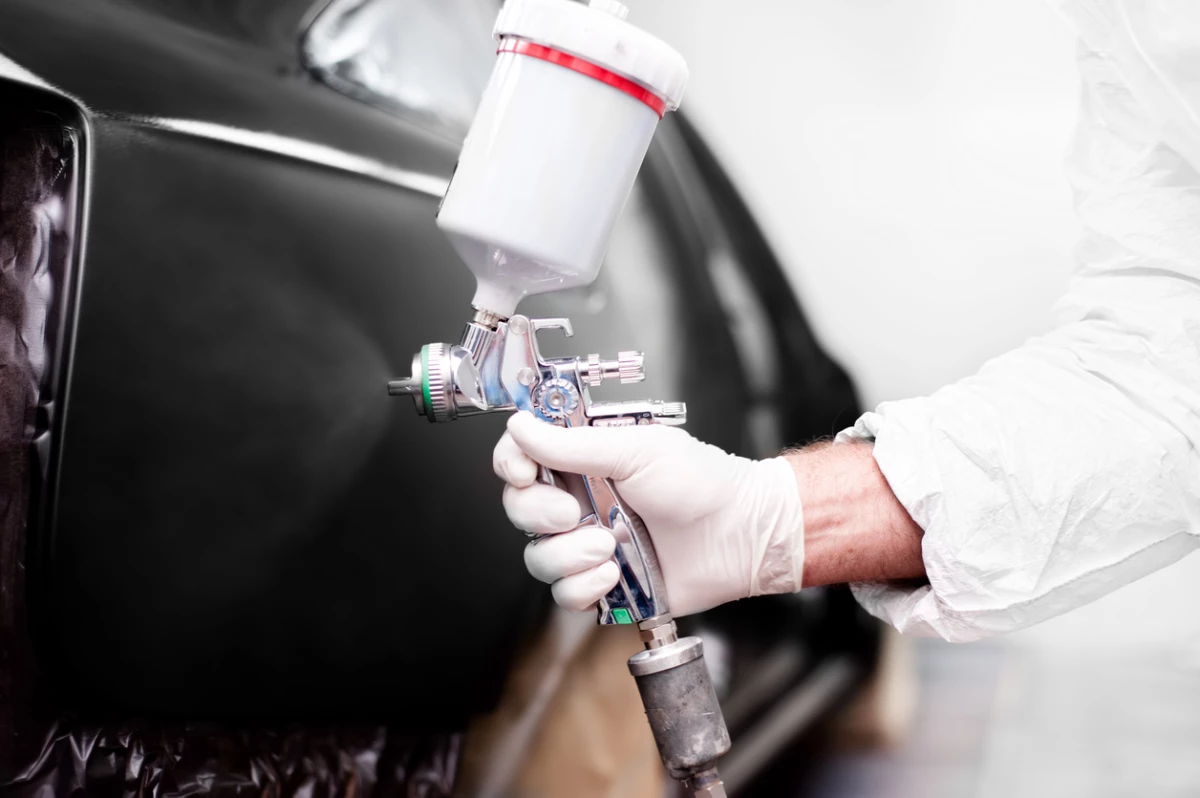 Worker using paint spray gun for painting a car