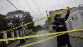 Un oficial de policía acordona una calle donde un poste de línea eléctrica se apoya en una casa después de la tormenta tropical Ernesto en Fajardo, Puerto Rico, el 14 de agosto de 2024.