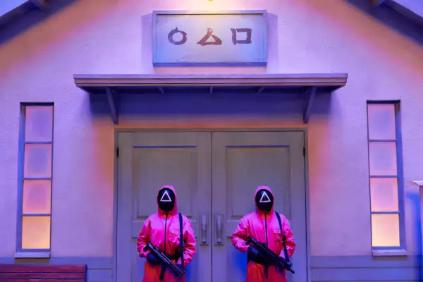 Foto de una escena del Juego del Calamar con dos guardias armados que llevan mono rosa y máscaras vigilando una puerta.