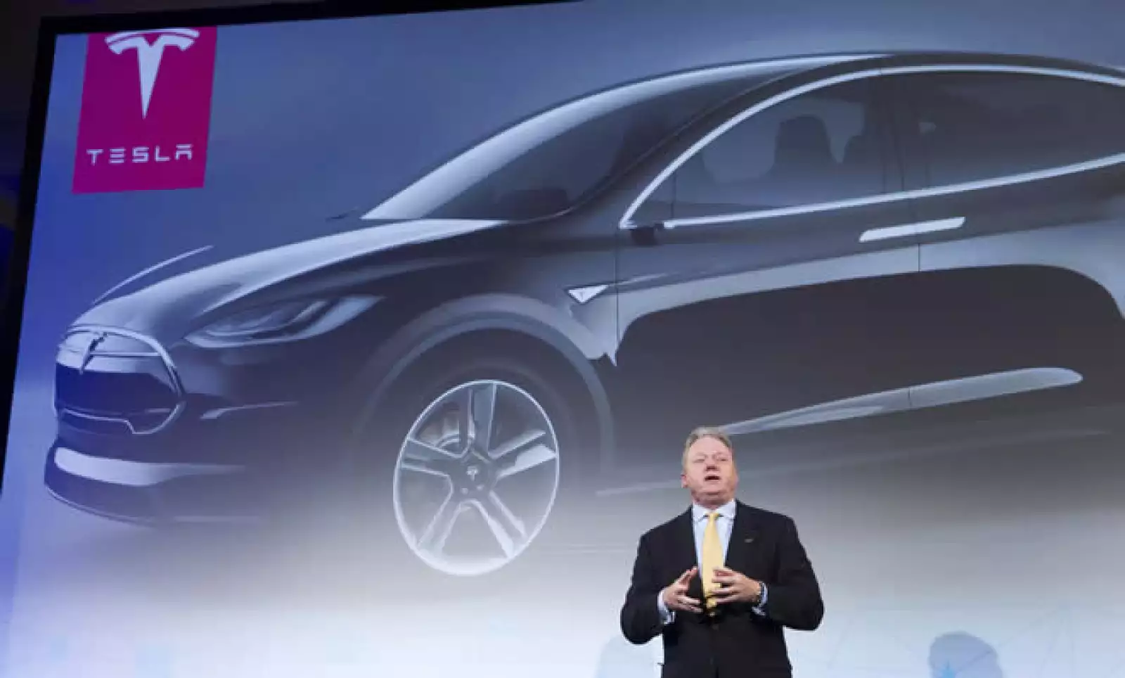 Joseph taylor, CEO de Panasonic para Norteamérica, habla frente a una imagen del Tesla, un auto eléctrico. La firma y Tesla están asociados con Gigafactory, fabricante de baterías.