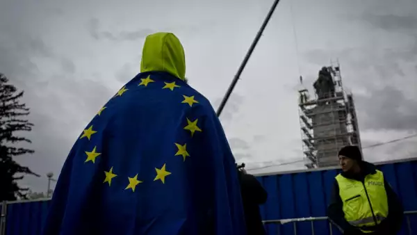Un hombre envuelto en la bandera de la Unión Europea observa cómo los trabajadores se preparan para desmentir un monumento del ejército soviético que representa tres esculturas de bronce de un soldado soviético, un trabajador y una madre y su hijo, en Sofía, el 13 de diciembre de 2023.