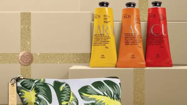 Tres envases de cremas de manos de la línea Ekos de Natura en envases color amarillo, naranja y rojo. Se ubican sobre una caja de cartón. 