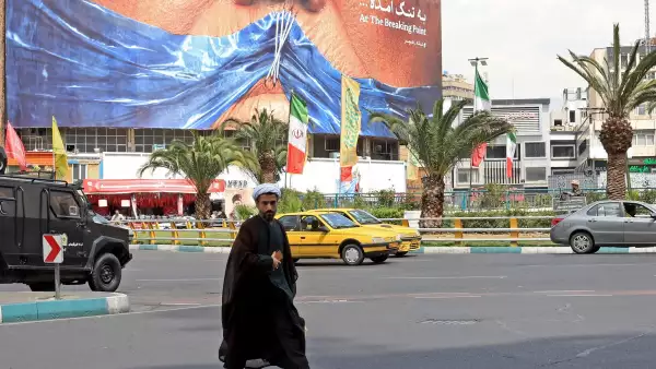 Un clérigo iraní pasa junto a una valla publicitaria antiestadounidense que se refiere al presidente Donald Trump y al estrecho de Ormuz, instalada en un edificio en la plaza Valiasr en Teherán el 2 de mayo de 2026.