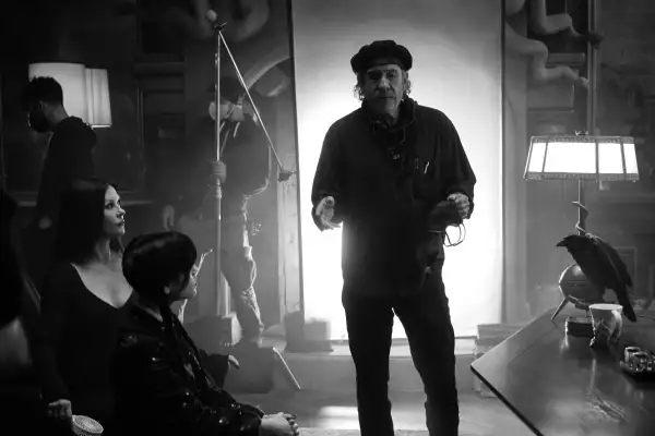Foto en blanco y negro de Tim Burton hablando con Jenna Ortega y Catherine Zeta-Jones en el set de Merlina.