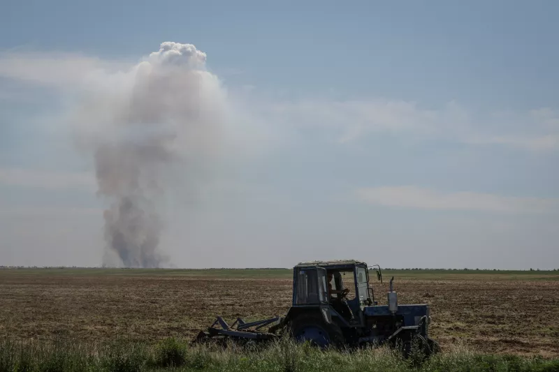 Un trabajador agrícola opera un tractor a medida que el humo aumenta en la distancia después de un ataque militar, en medio del ataque de Rusia contra Ucrania, en la región de Kherson, Ucrania, el 20 de junio de 2023.