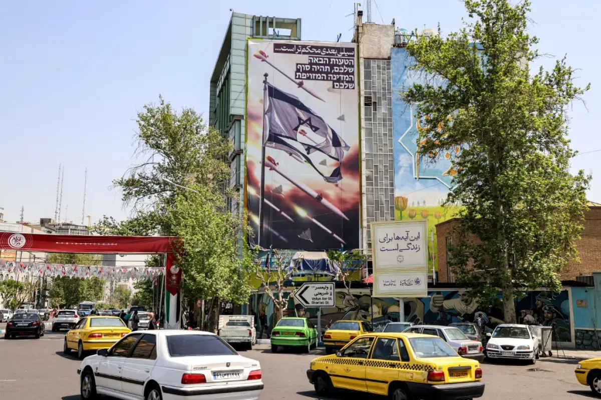 El vehículo pasa por un edificio que muestra una pancarta que representa misiles y drones volando más allá de una bandera israelí desgarrada, con el texto en persa que dice "la próxima bofetada será más difícil" y en hebreo "tu próximo error será el fin de tu estado falso", en la Plaza de Palestina en Teherán el 14 de abril de 2024.