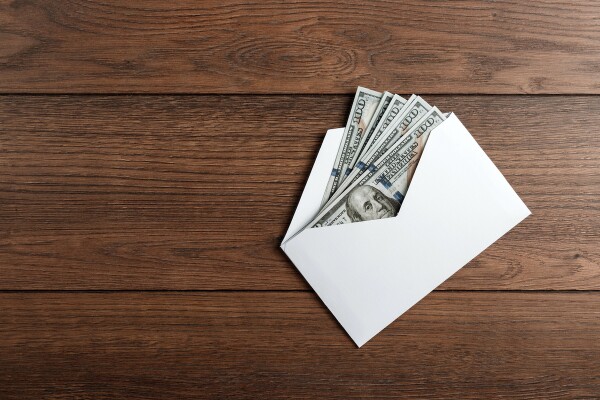 US dollars in a white envelope on a wooden table. The concept of income, bonuses or bribes. Corruption, salary, bonus.