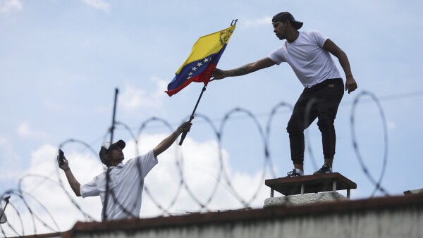 A man gives a flag of Venezuela to one another, on the roof of the Consulate of Venezuela, during a protest in Bogota