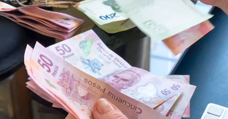 Una mano sostiene un fajo de billetes de 50 y 200 pesos mexicanos.jpg