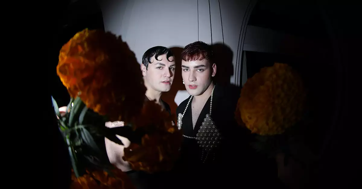 Dos visitantes de la Ofrenda de Muertos de Jean Paul Gaultier, en primer plano flores de cempasúchil. 