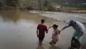 Héctor Ojeda, Sonia Robles y Tony Ojeda se preparan para cruzar un río a pie después de que el puente fuera arrastrado cuando el huracán María pasó el 27 de septiembre de 2017 en Morovis, Puerto Rico. Puerto Rico sufrió daños generalizados y graves, incluyendo la mayoría de las redes eléctricas, de gas y de agua, así como la destrucción agrícola después de que pasara el huracán María, un huracán de categoría 4.
