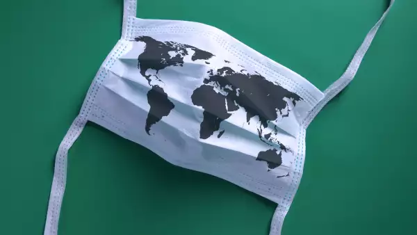 White face mask with a map of the world is lying on a green background