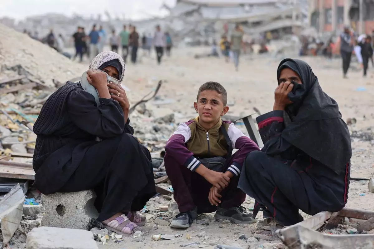 Mujeres palestinas y un niño miran mientras la gente se une para recoger paquetes de alimentos después de que los camiones de ayuda entraran desde el cruce de Karem Abu Salem, en Khan Yunis, en el sur de la Franja de Gaza, el 12 de octubre de 2025, mientras se celebra un alto el fuego entre Israel y las facciones palestinas en el territorio sitiado.