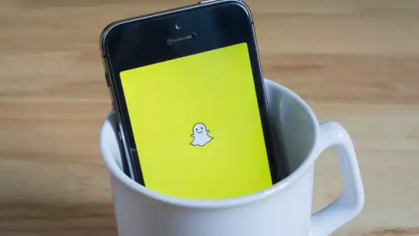 Apple iPhone5s in a mug showing its screen with Snapchat logo.
