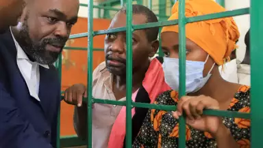 Paul Mackenzie, de 50 años, un líder de culto keniano acusado de ordenar a sus seguidores, que eran miembros de la Iglesia Internacional de las Buenas Noticias, que murieran de hambre en el bosque de Shakahola, y su esposa Rhoda Mumbua Maweu, hablan con su abogado George Kariuki desde un muelle a la parrilla de acero en los tribunales de abogados de Shanzu