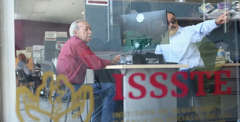 Adulto mayor frente a un trabajador del ISSSTE en las oficinas de la dependencia.