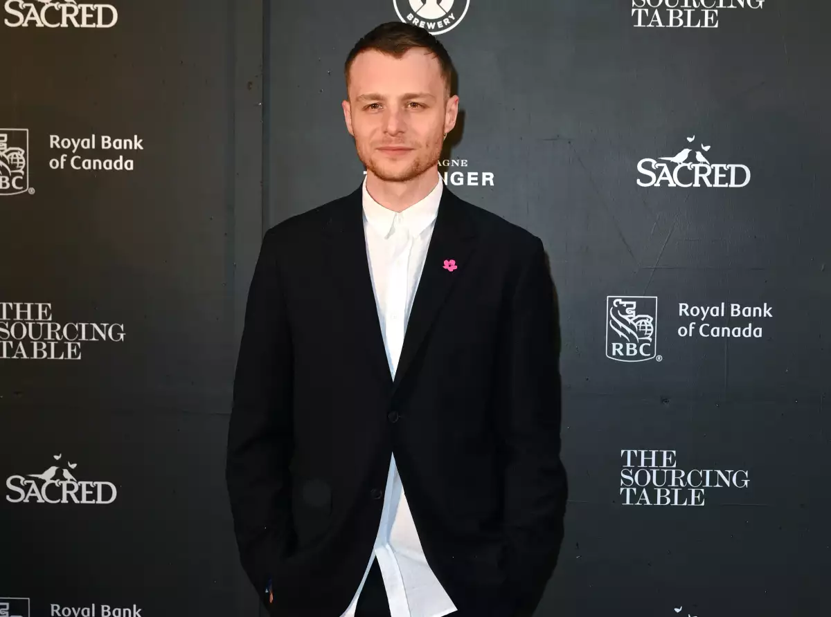 Foto del actor Luke Thallon vestido de camisa blanca y saco negro.