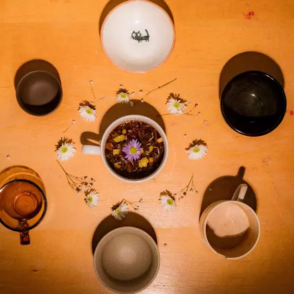 Foto de seis tazas vacías acomodadas en círculo y al centro una taza llena de té con flores alrededor.