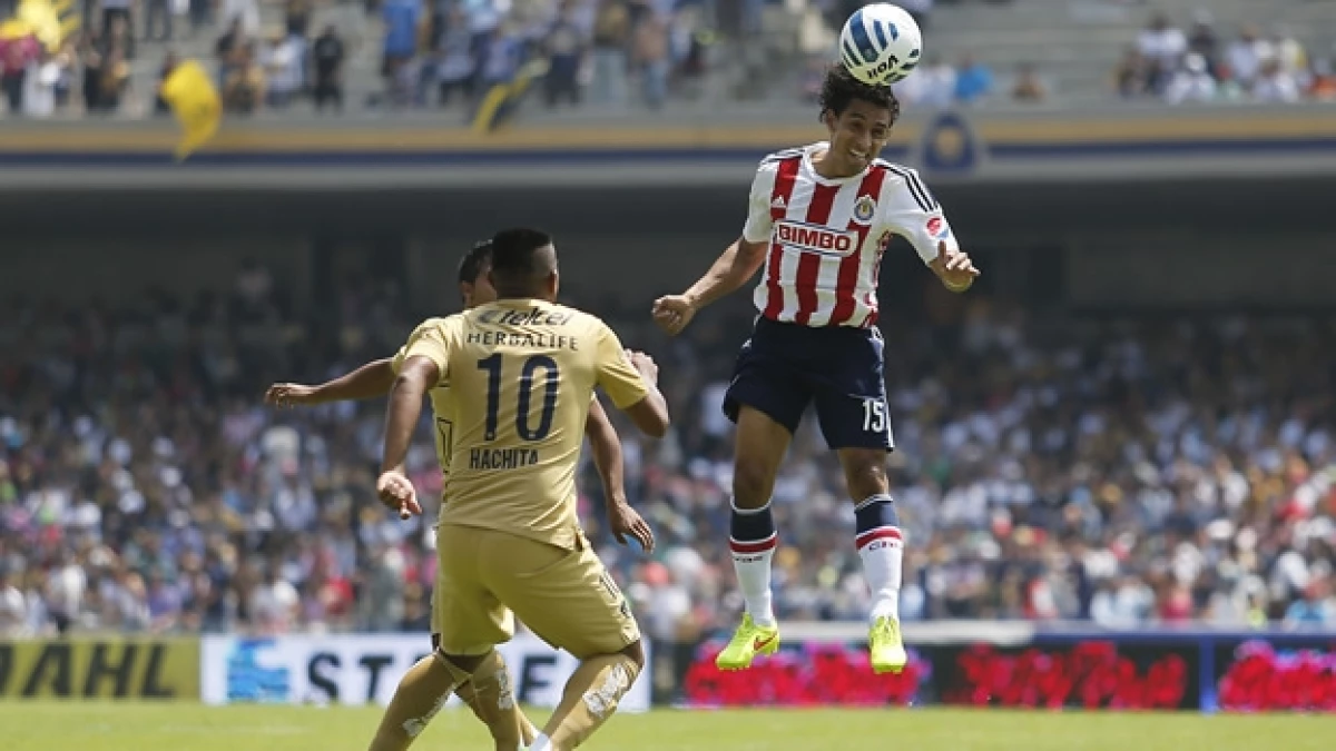 Fernando Arce de Chivas conecta el balón con la cabeza ante la marca de los jugadores del cuadro universitario