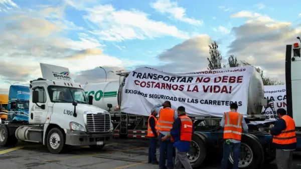 Transportistas frente a sus camiones durante el paro nacional de este 26 de octubre. En uno de los camiones cuelga una manta que dice "Transportar no debe costarnos la vida". 