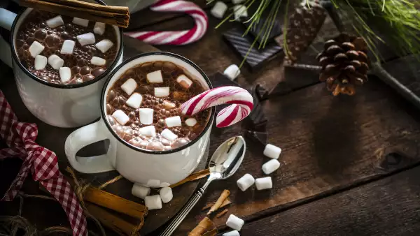 Two homemade hot chocolate mugs with marshmallows on rustic wooden Christmas table