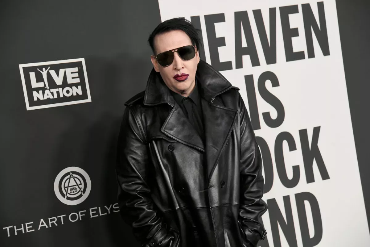 Foto de Brian Warner, conocido como Marilyn Manson, vestido con chaqueta negra de piel, lentes oscuros y boca pintada de rojo a la entrada del evento anual The Art of Elysium, en 2020.