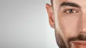 Foto de la mitad de la cara de un hombre con barba y piel limpia