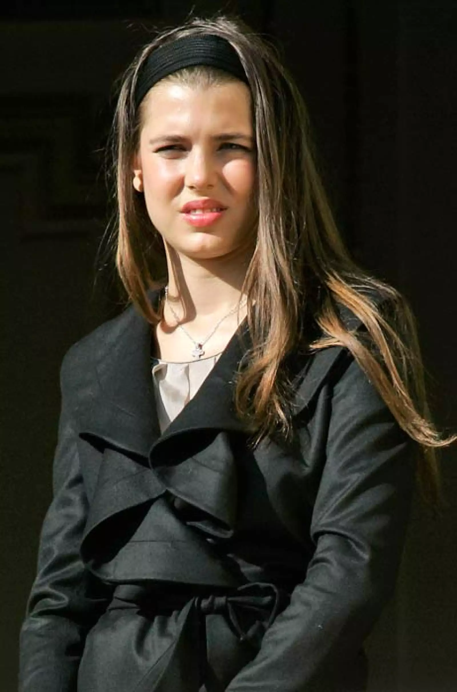 Más pequeña con un trench coat negro de holanes y el pelo suelto y lacio.