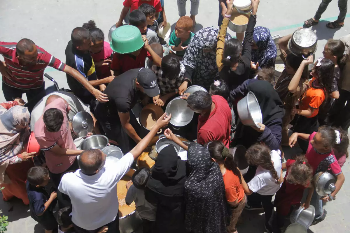 Los palestinos se reúnen para recibir comida cocinada en una cocina benéfica, mientras luchan contra la escasez de alimentos, necesidades básicas en medio del conflicto entre Israel y Hamas, en el campo de refugiados de Jabalia, en el norte de la Franja de Gaza, el 19 de junio de 2024.