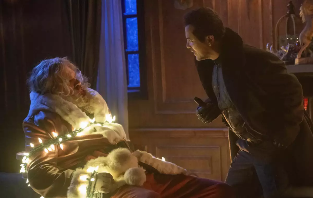 foto de una escena de la película 'Navidad sin Paz' con Santa Claus amarrado con una serie de luces encendidas y enfrente de él un ladrón.