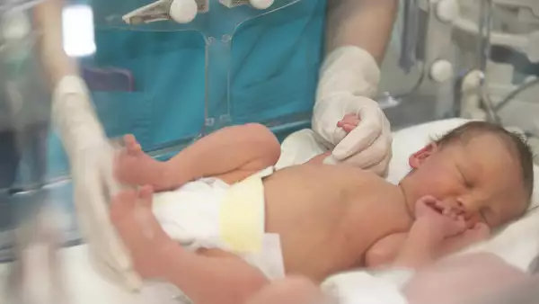 Las manos del médico con guantes de goma sostienen los dedos pequeños de un bebé recién nacido que está acostado en la caja médica.
