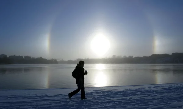 Una mujer pasea a orillas del lago Malaren con el fenómeno atmosférico Parhelio visto al fondo