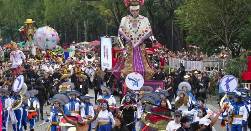 Dos catrinas gigantes con huipiles. Hombres y mujeres vestidos de blanco y azul con maquillaje de catrinas.jpg