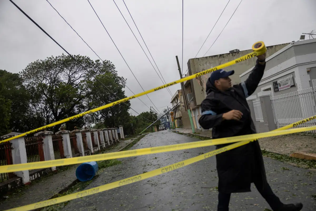 Un oficial de policía acordona una calle donde un poste de línea eléctrica se apoya en una casa después de la tormenta tropical Ernesto en Fajardo, Puerto Rico, el 14 de agosto de 2024.
