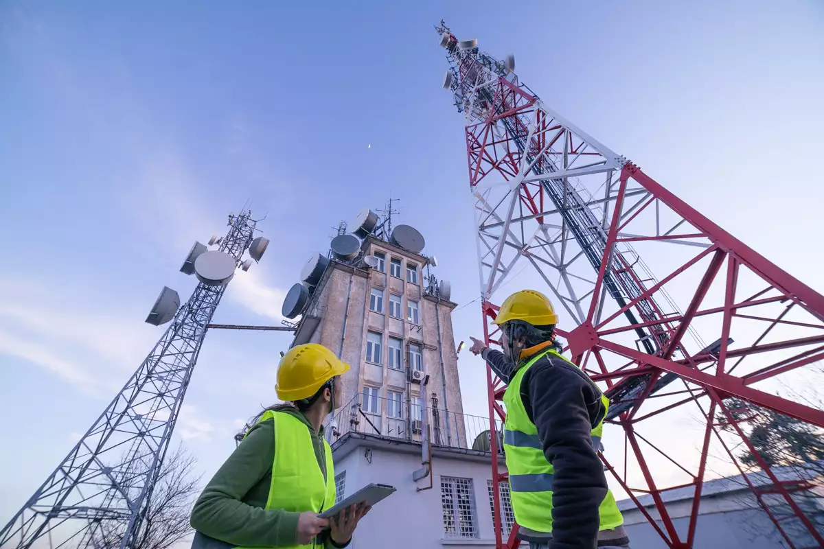 (Ingenieros trabajando frente a una torre de telecomunicaciones)