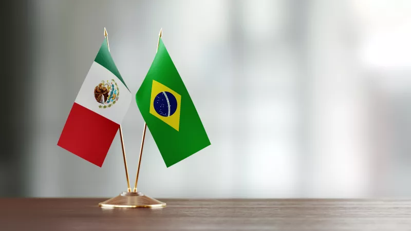 Mexican And Brazilian Flag Pair On A Desk Over Defocused Background