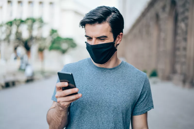 Man with protective mask using smartphone outdoors in the city.