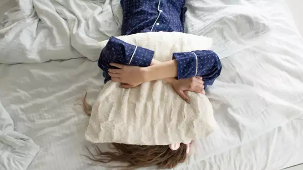 Too lazy to get out of bed, a woman covers her face with a pillow