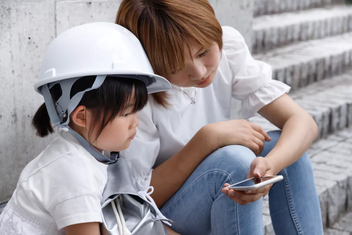 Una niña pequeña y su madre usando cascos operan teléfonos inteligentes. Imagen de control de seguridad durante un desastre.