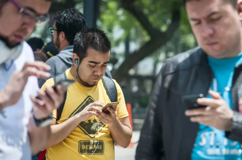 Tres personas sostienen sus teléfono celulares mientras caminan por la calle.