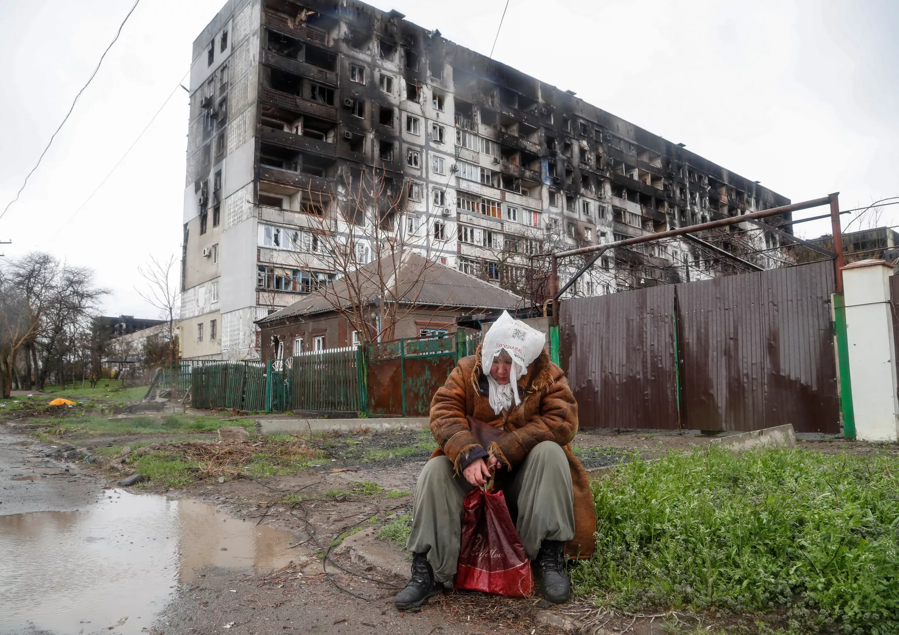 Una mujer se sienta frente a un edificio residencial dañado en el curso del conflicto entre Rusia y Ucrania en un día lluvioso en la ciudad portuaria de Mariupol en el sur de Ucrania. 