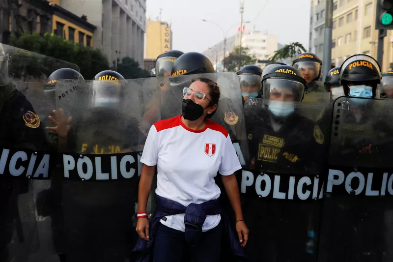 Una manifestante se para en frente de oficiales de policía después que el presidente Pedro Castillo impuso un toque de queda en la capital lima. 