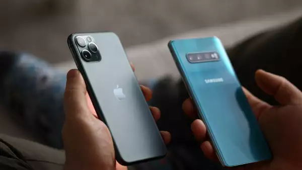 Persona sosteniendo dos teléfonos: un iPhone y un Samsung boca abajo, donde se pueden ver sus marcas.