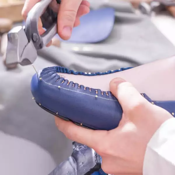 Luego de posicionar la parte superior del zapato sobre la suela de goma, la monta con pegamento. Enseguida, asegura la silueta del zapato clavando delicadas y pequeñas tachuelas.