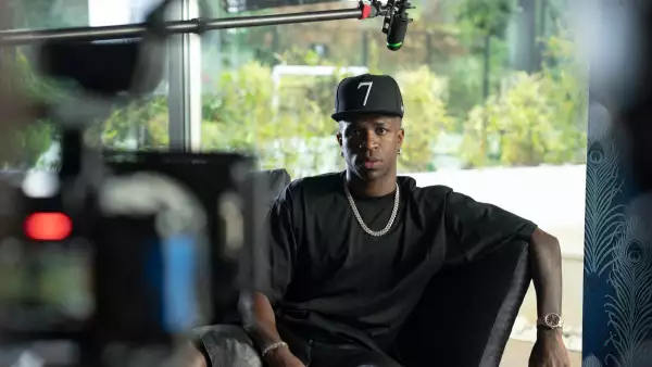 Foto de Vinicius Jr vestido casual de negro con gorra y frente a la cámara de cine que graba su documental.