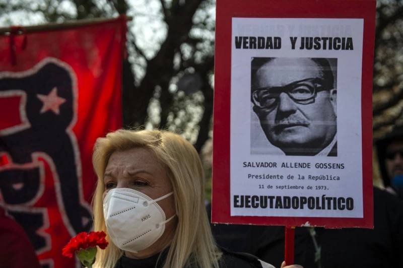 Una mujer con cubrebocas sontiene una pancarta con la foto de Salvador Allende.