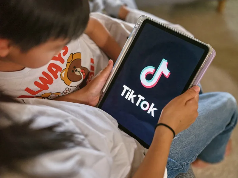Dos menores de edad miran la pantalla de una tableta donde aparece el logo de TikTok. 