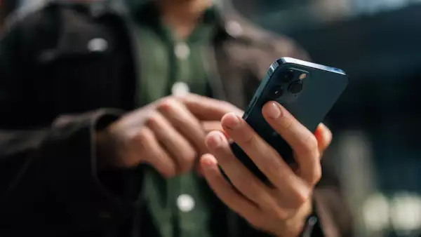 Close-up hands of unrecognizable man holding and using smartphone standing on city street, browsing internet, checking social media, using mobile application.