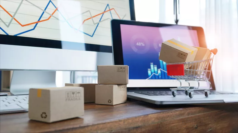 Online shopping, Boxes on table and in trolley on a laptop keyboard and business graph growth on screen background, Electronic commerce.